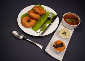 A classic South Indian breakfast featuring vadai served with sambar and chutneys on a black background.