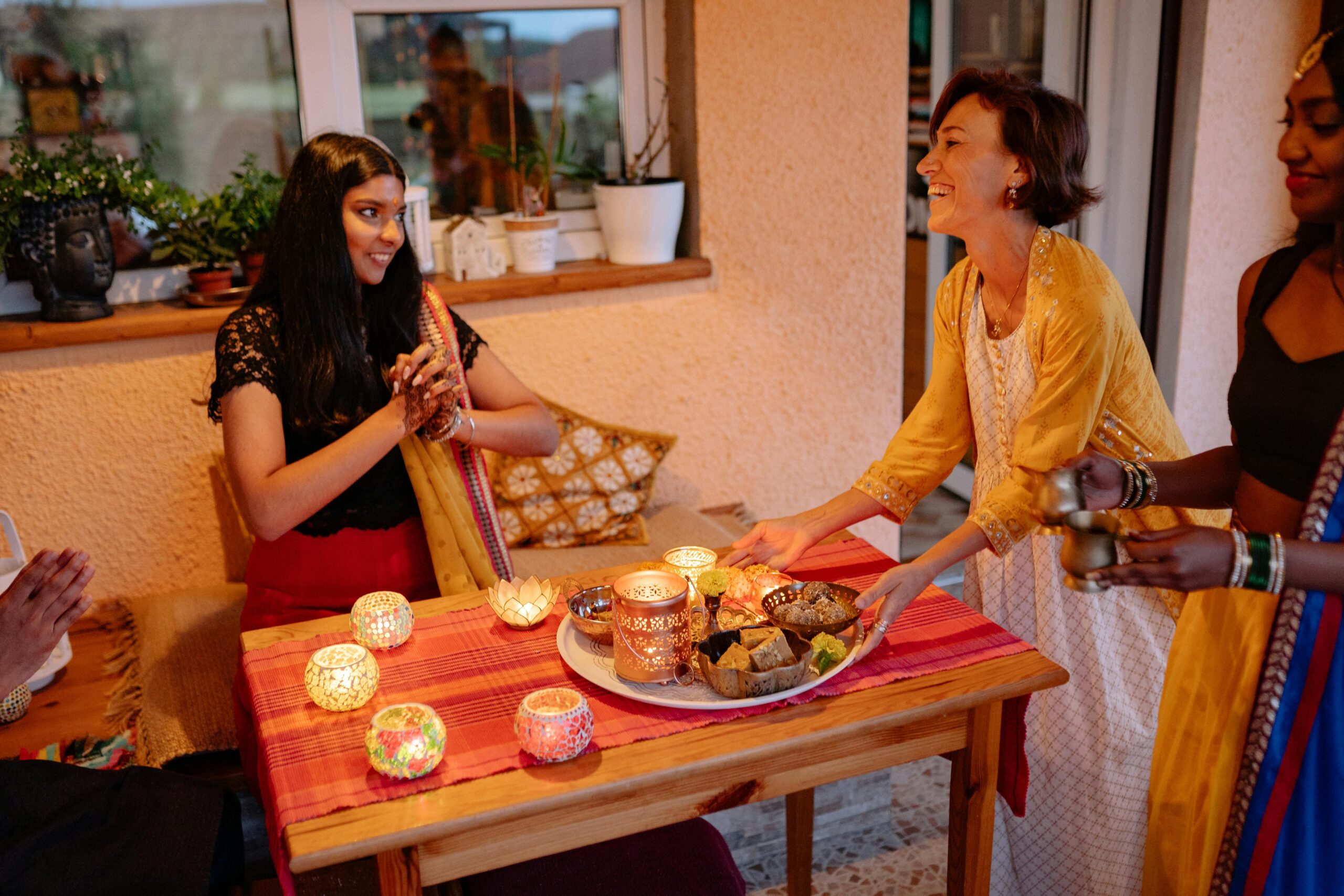 South Asian women celebrating Diwali with traditional attire and sweets indoors.