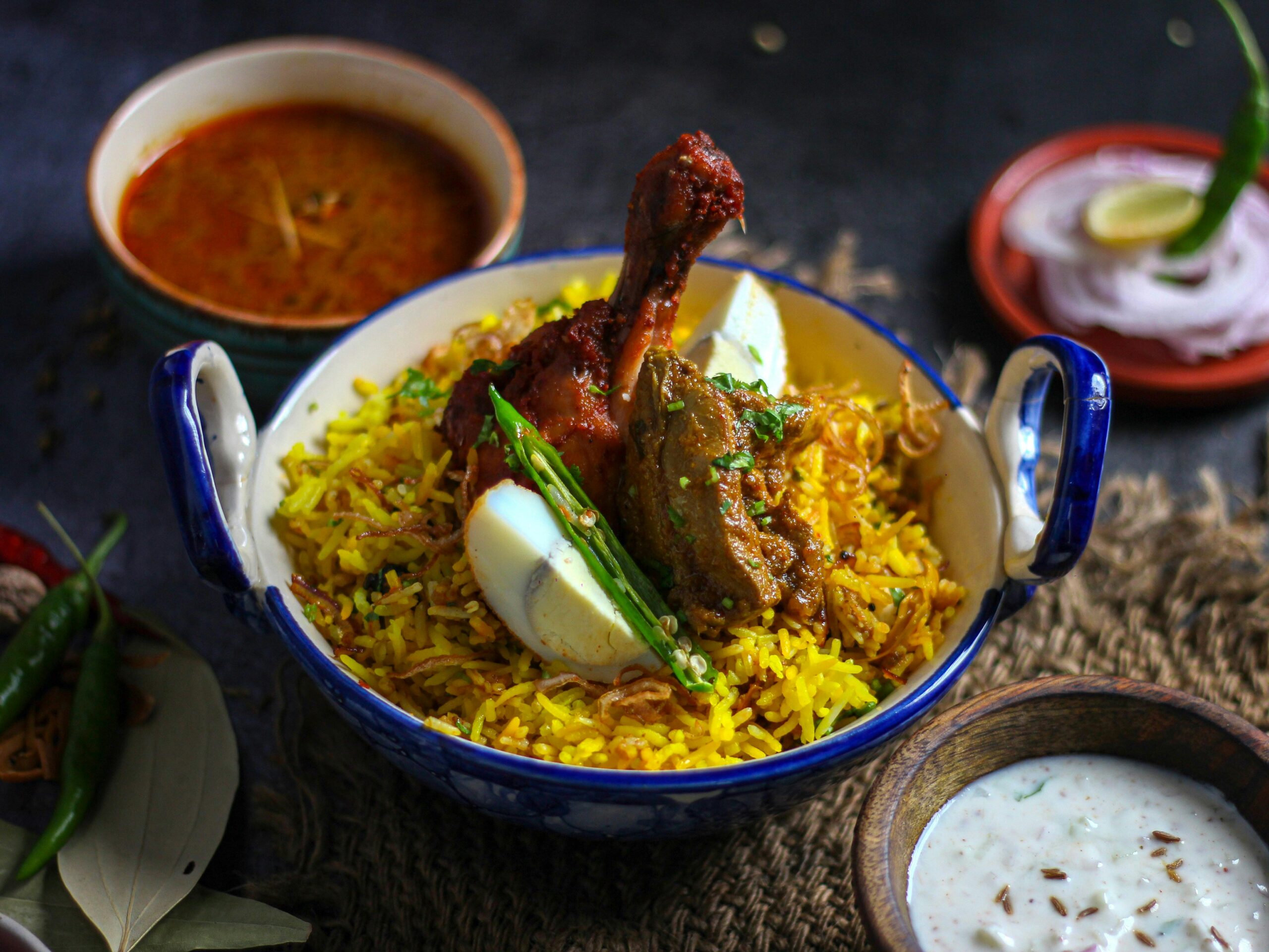 A delicious Indian chicken biryani with eggs, garnished with chilies, served with curry sauce and raita.